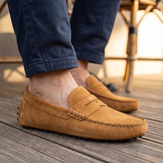 mocassin en daim camel porté avec un chino marine sur le platelage bois d'une terrasse de café