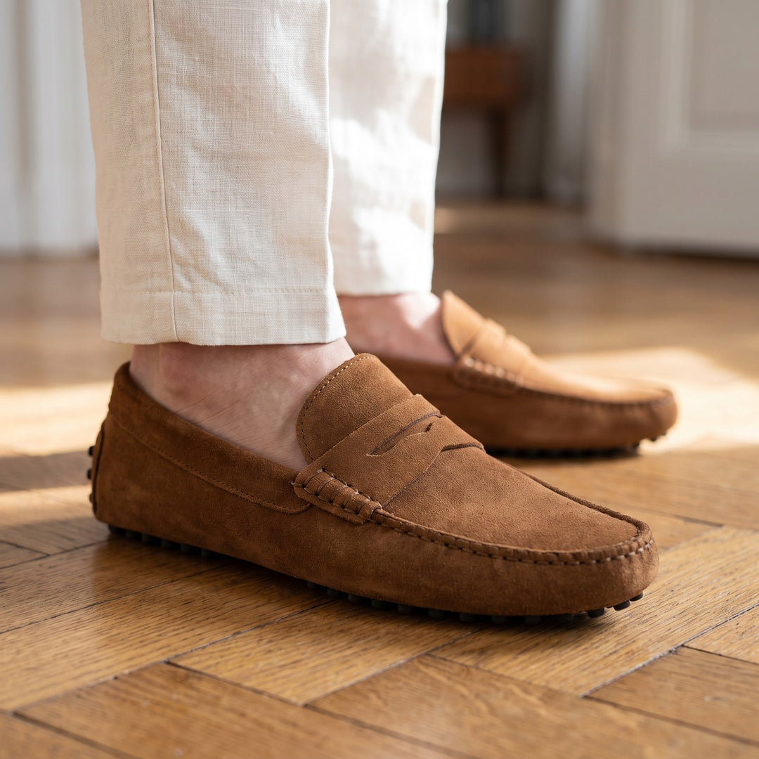 mocassin en daim marron porté avec un pantalon de lin écru sur un parquet ancien en chevrons