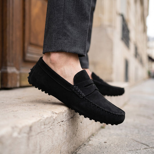 mocassin en daim noir porté avec un pantalon de costume anthracite sur une marche en pierre