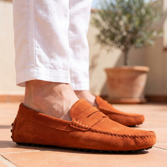 mocassin en daim orange porté avec un pantalon de lin blanc sur une terrasse en terre cuite