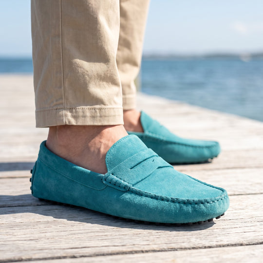 mocassin en daim turquoise porté sur les planches de bois clair d'un ponton en bord de mer