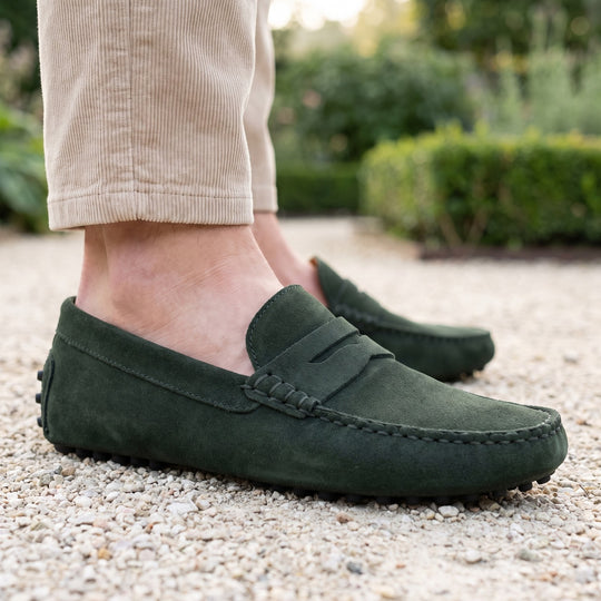mocassin en daim vert foncé porté avec un pantalon de velours beige sur une allée de gravier